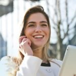 Confident businesswoman using her tablet and phone, smiling outdoors in sunlight.