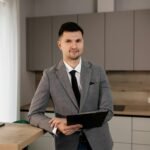 Confident real estate agent holding a clipboard in a stylish office setting, ready to assist clients.